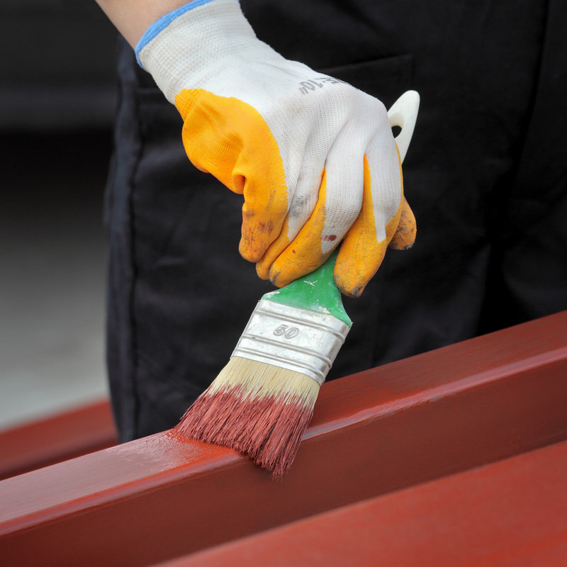 Worker painting steel tube with paint brush selective focus on hand